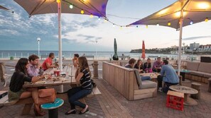 An outdoor seating area with tables and chairs, a view of the sea, and a cityscape in the background. - Luxe 2BR w Smart TV Steps from Bondi Beach (North Bondi)