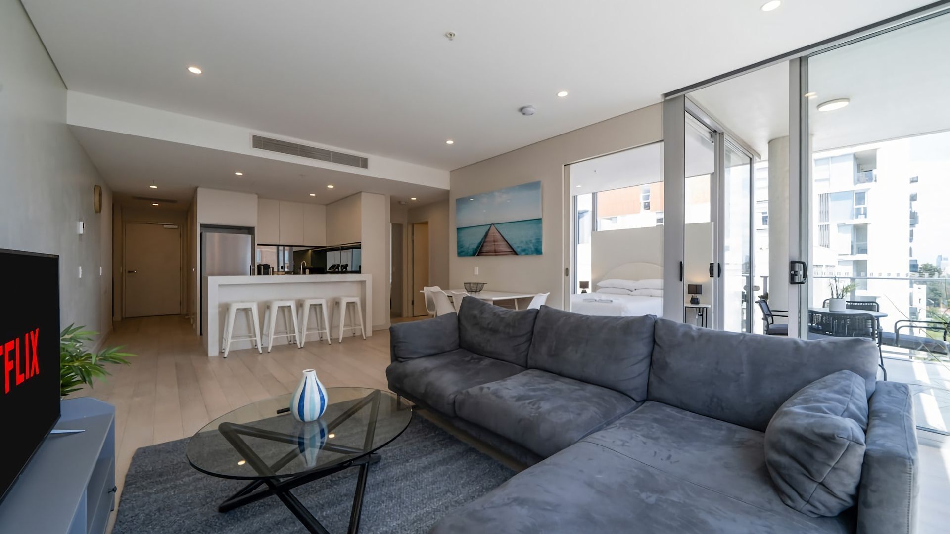 A modern living room with a grey sofa, a glass coffee table, and a TV.