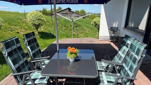Un patio exterior con una mesa y cuatro sillas, una planta en maceta y vistas a un paisaje rural.