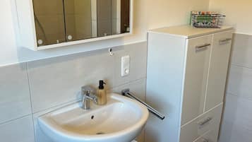 Un baño moderno con lavamanos blanco, espejo, ducha y un armario con cajones.
