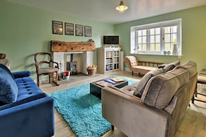 A living room with a fireplace, a bookshelf, and a window with a view. - Cottage in Carhampton Near Dunster Castle (Minehead)