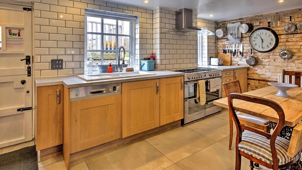 A kitchen with wooden cabinets, a gas stove, a sink, and a dining area with a table and chairs.