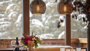 Ein gemütlicher Essbereich mit einem Holztisch, gedeckt für eine Mahlzeit, inklusive Weinflasche, Gläsern, einer Vase mit Blumen und Kerzen.