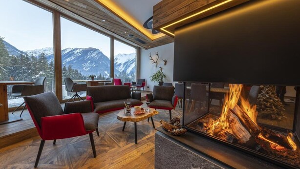 Ein modernes Wohnzimmer mit Kamin, großen Fenstern und Blick auf schneebedeckte Berge.