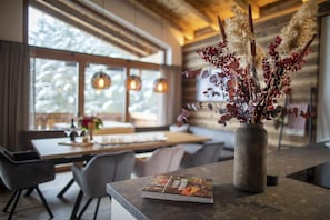 Un intérieur moderne avec un plafond en bois, une grande fenêtre donnant sur les arbres et un vase contenant des plantes séchées, posé sur un comptoir.