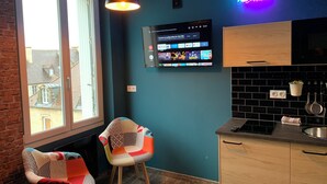 A modern kitchen with a large window, a colorful chair, a mounted TV, and a neon sign. - ★ Studio Grévy ★ fully equipped - Heart of downtown - Wifi fiber - Netflix (Dole)