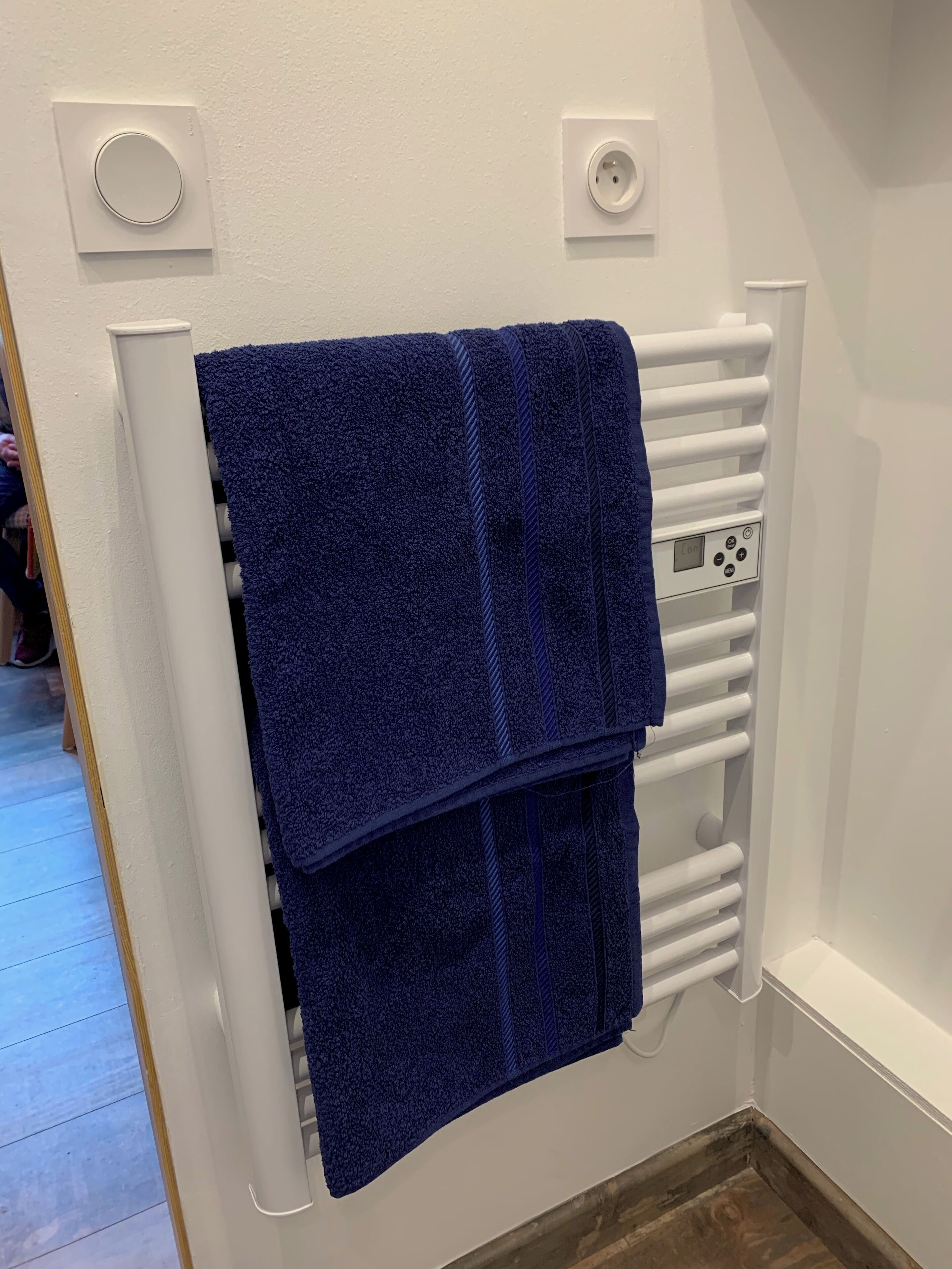 Ett badrum med ett vitt element, en blå handduk och en kontrollpanel.