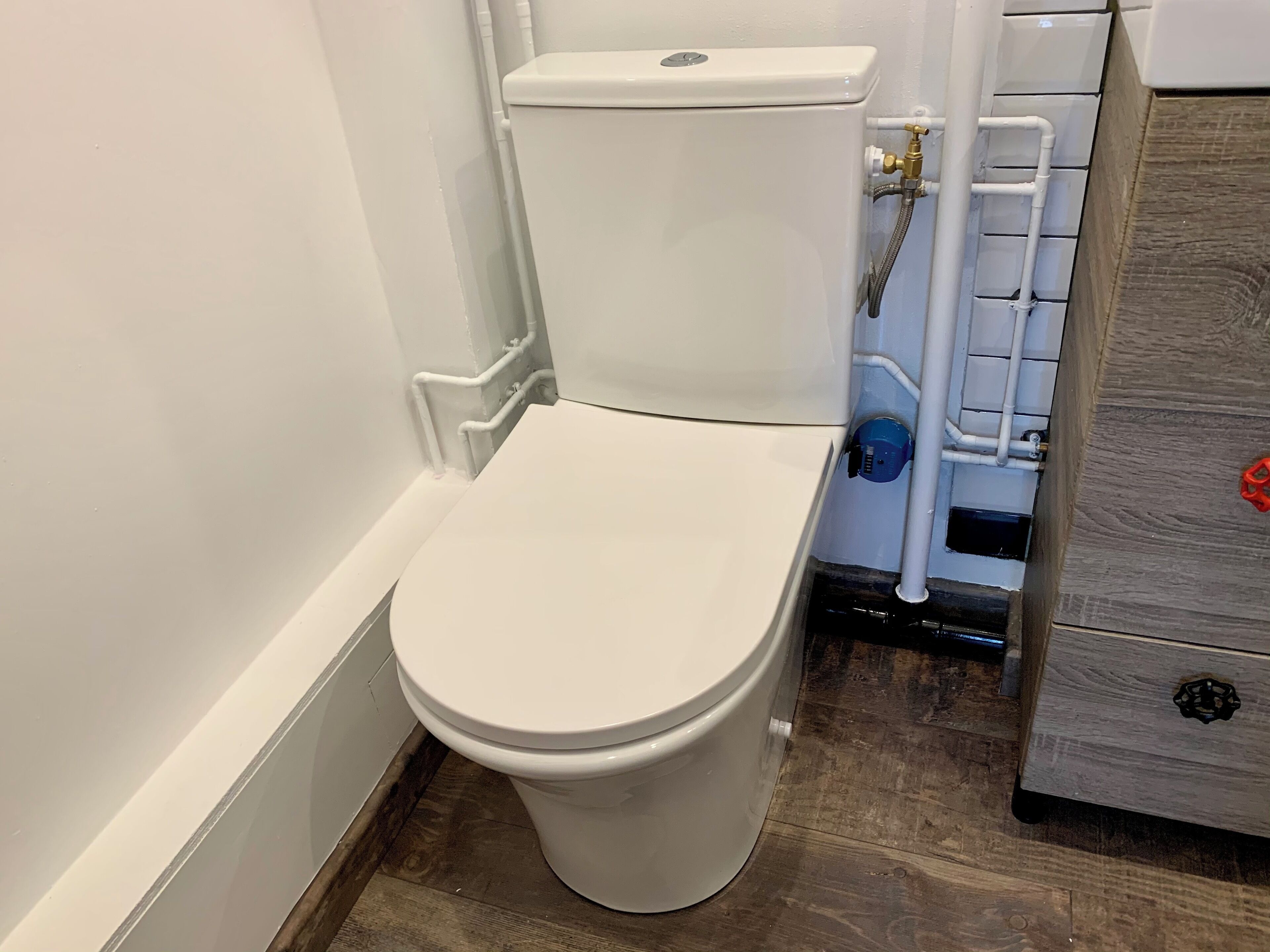 Un inodoro blanco con tanque, un mueble de madera con cajón y una tubería de metal.