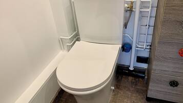 Un inodoro blanco con tanque, un mueble de madera con cajón y una tubería de metal.