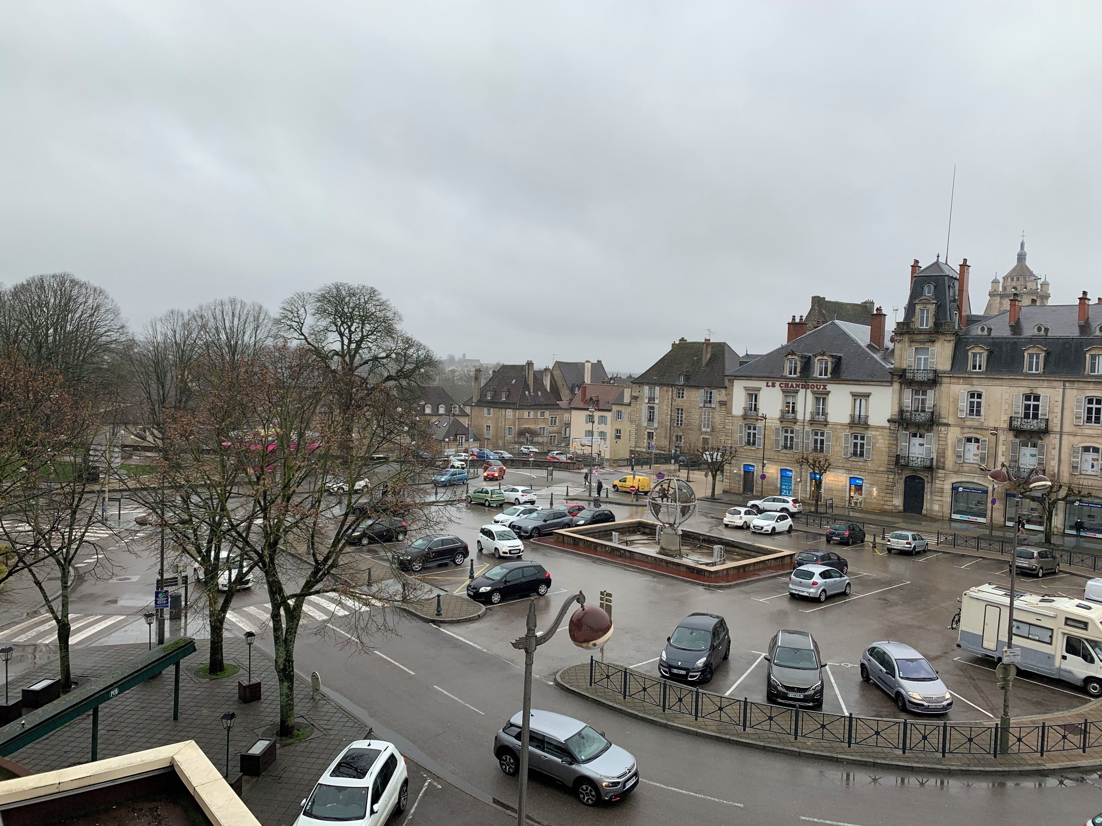 Une rue de la ville bordée de voitures garées, avec un rond-point et des bâtiments historiques.