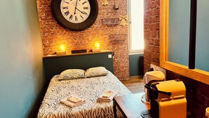 A hotel room with a brick wall, a bed with patterned bedding, a clock, and a massage chair. - ★ Studio Grévy ★ fully equipped - Heart of downtown - Wifi fiber - Netflix (Dole)