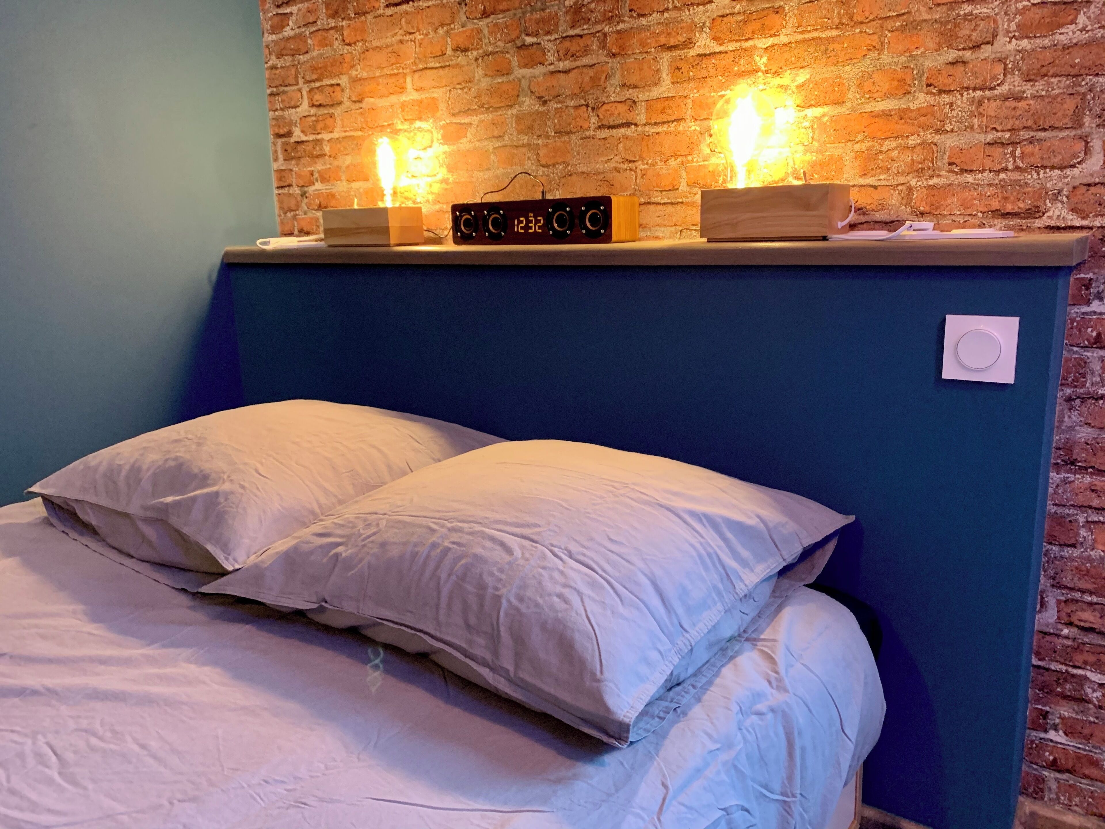 Una cama con sábanas blancas y una pared de ladrillo detrás.