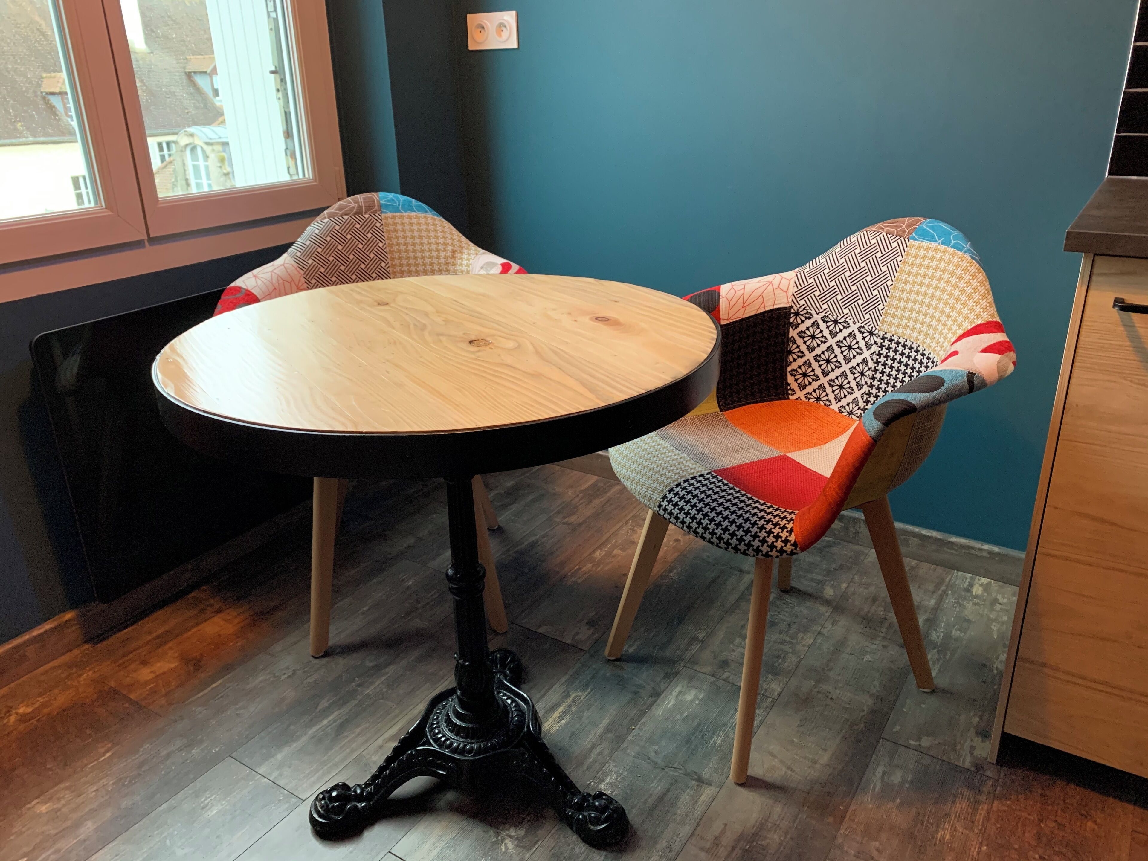 A round wooden table with a black metal base, positioned between two chairs with patterned upholstery.