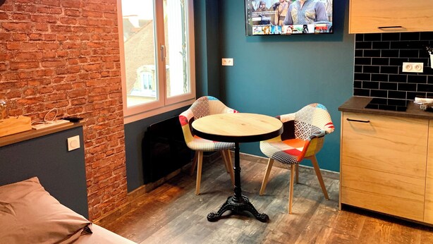 A cozy room with a brick wall, a wooden table with two chairs, a TV on the wall, and a neon sign. - ★ Studio Grévy ★ fully equipped - Heart of downtown - Wifi fiber - Netflix (Dole)