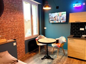 A cozy room with a brick wall, a wooden table with two chairs, a TV on the wall, and a neon sign. - ★ Studio Grévy ★ fully equipped - Heart of downtown - Wifi fiber - Netflix (Dole)
