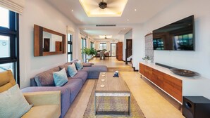 A modern living room with a sectional sofa, a coffee table, a TV mounted on the wall, and a staircase leading to another level. - Patak 3 Bedroom Private Pool Villa (Karon)