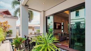 A modern outdoor patio with potted plants, a seating area, and a glass door leading to a living room with a sofa and a coffee table. - Patak 3 Bedroom Private Pool Villa (Karon)