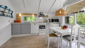 Une cuisine moderne avec des meubles blancs, une table à manger avec des chaises et une grande fenêtre qui laisse entrer la lumière naturelle.