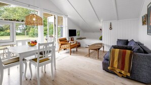 Un vaste espace de vie, décoré dans des tons de blanc, comprenant une table à manger, des chaises, un canapé et un téléviseur.