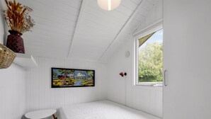 Une chambre à coucher avec un lit, une fenêtre, un tableau, une petite table et un vase contenant des fleurs séchées.