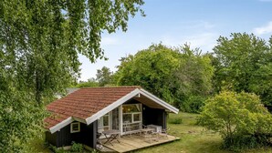 Une petite cabane avec un toit en pente, une terrasse et un espace patio aménagé avec du mobilier d’extérieur.
