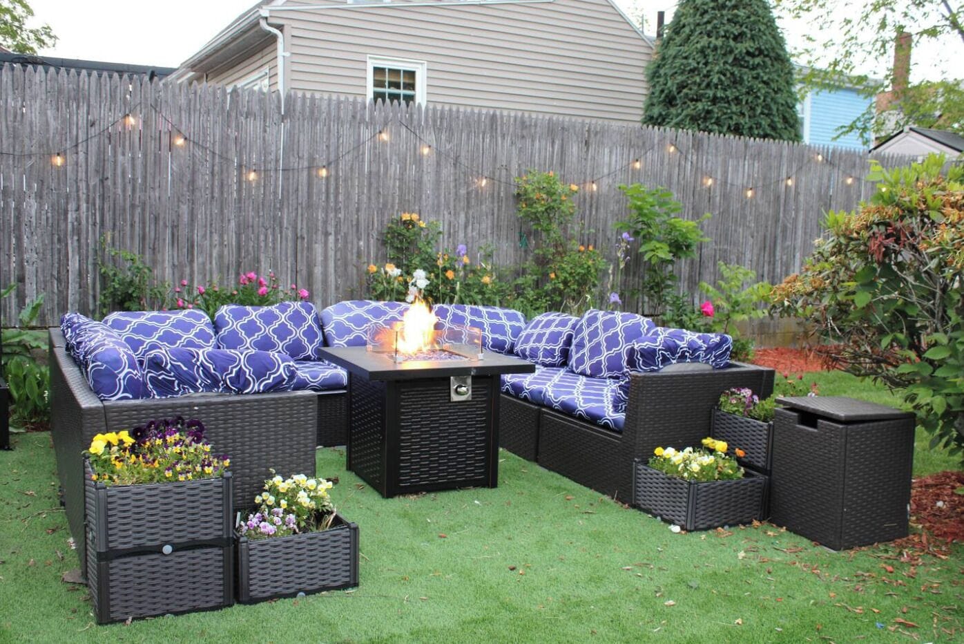 An outdoor patio with a sectional sofa, a fire pit, and planters with flowers.