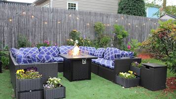 An outdoor patio with a sectional sofa, a fire pit, and planters with flowers.