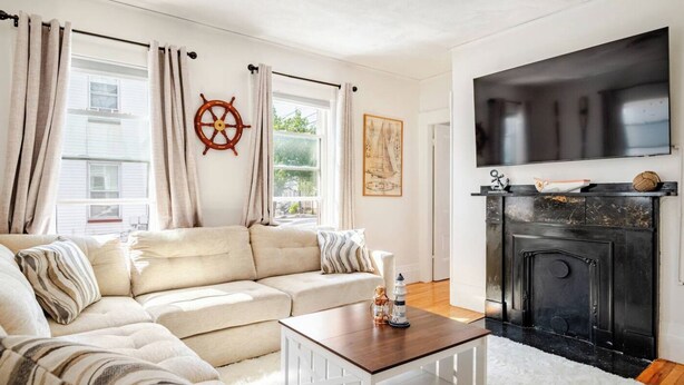 A living room with a beige sectional sofa, a wooden coffee table, a fireplace, and a mounted TV. - Witch City Retreat w/ Tiki Bar (Salem)