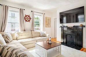 Un salon avec un canapé d’angle beige, une table basse en bois, une cheminée et un téléviseur fixé au mur.