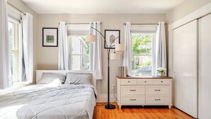 A bedroom with a bed, a dresser, a floor lamp, and a window with curtains. - Witch City Retreat w/ Tiki Bar (Salem)