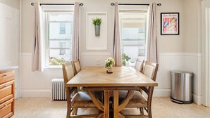 A dining room with a wooden table, beige chairs, a vase of flowers, and a radiator. - Witch City Retreat w/ Tiki Bar (Salem)