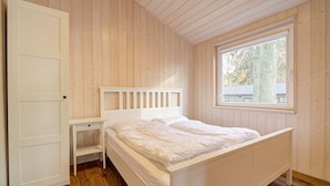 Makuuhuoneessa on puulattia, valkoinen sänky päätyineen, yöpöytä ja ikkuna, josta avautuu näkymä puihin.