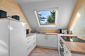 A kitchen with white cabinets, a countertop, a window, and a view of trees.