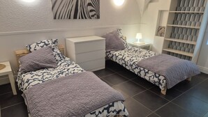 Una habitación con dos camas, cada una con colcha y almohadas estampadas, una mesita de noche con lámpara, un aparador y un cuadro con estampado de cebra colgado en la pared.