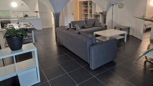 Una sala moderna con un sofá gris, una mesa de centro blanca y una zona de comedor con una cocina al fondo.