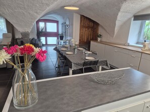 Un coin repas avec une table dressée pour quatre personnes, un vase rempli de fleurs et une cuisine en arrière-plan.