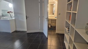 Una cocina moderna con baldosas oscuras, una puerta blanca y un pasillo que conduce a un baño con espejo e iluminación.