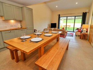 Un coin repas avec une table en bois dressée pour quatre personnes, un banc et un canapé en arrière-plan.