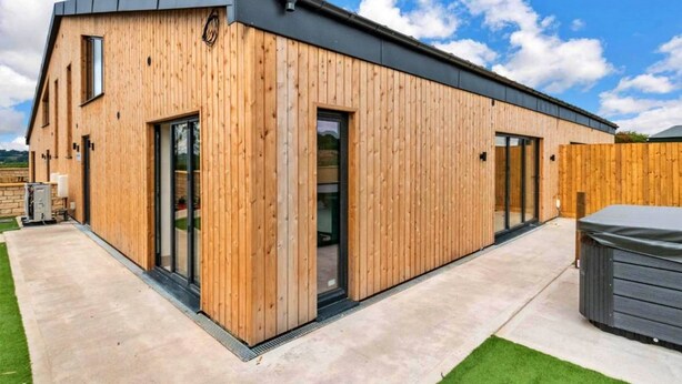 Un bâtiment moderne en bois, doté de grandes portes vitrées, d’une terrasse en béton et d’une clôture en bois.