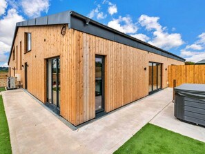 Un edificio moderno in legno con ampie porte vetrate, un patio in cemento e una recinzione in legno.
