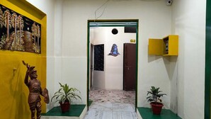 A hallway with a green carpet leading to a door marked G-2, flanked by potted plants and a statue. - Hotel Kashi Paradise (Varanasi)