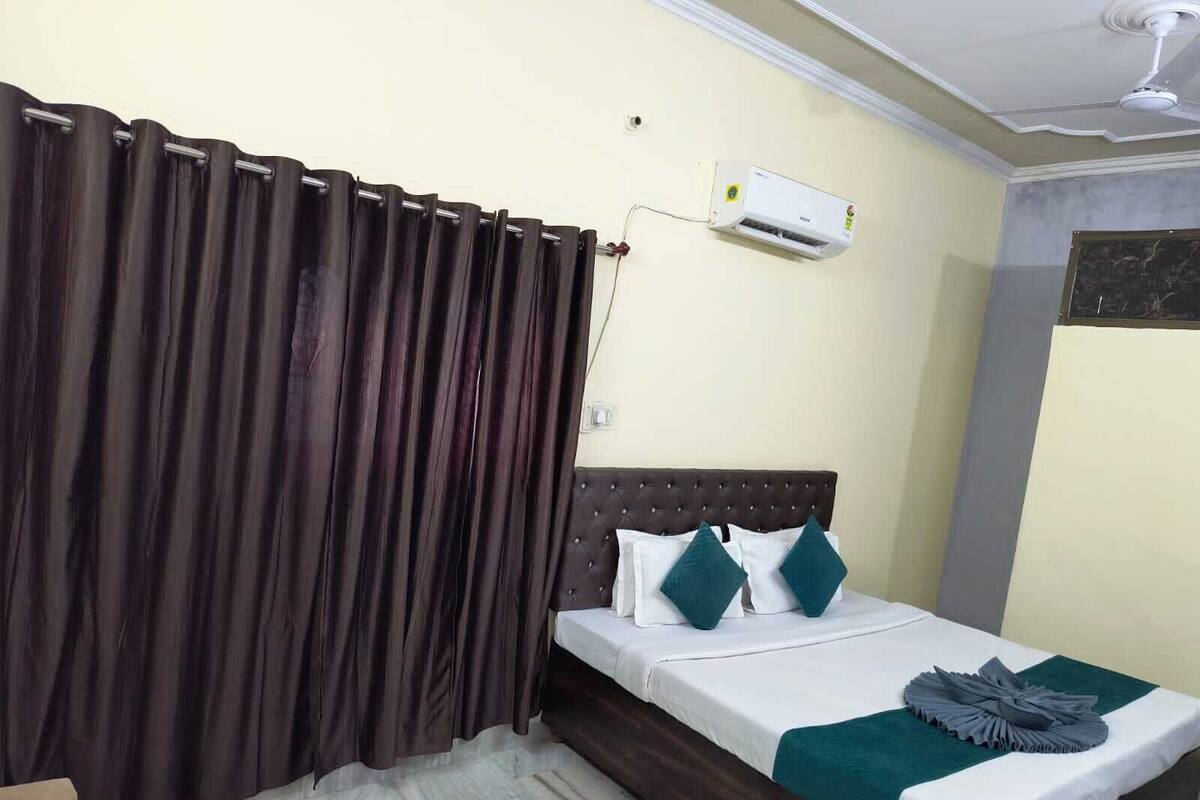 A bedroom with a bed, dark curtains, an air conditioning unit, and a ceiling fan.