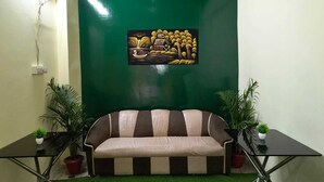 A room with a green wall, a sofa, two potted plants, and a painting. - Hotel Kashi Paradise (Varanasi)