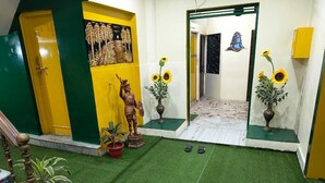 A room with artificial green carpet, a statue, a vase with sunflowers, and a mural on the wall. - Hotel Kashi Paradise (Varanasi)