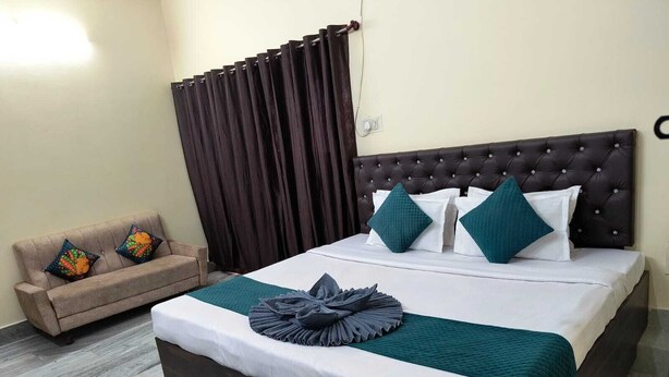 A neatly arranged hotel room with a large bed, a sofa, and a curtain. - Hotel Kashi Paradise (Varanasi)