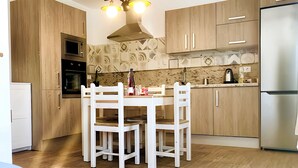 A modern kitchen with wooden cabinets, a white dining table, and a stainless steel refrigerator.