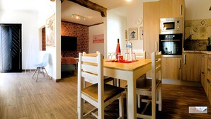 A modern kitchen with wooden cabinets, a built-in microwave, and an oven. There is a dining table with chairs and a small kitchen island.