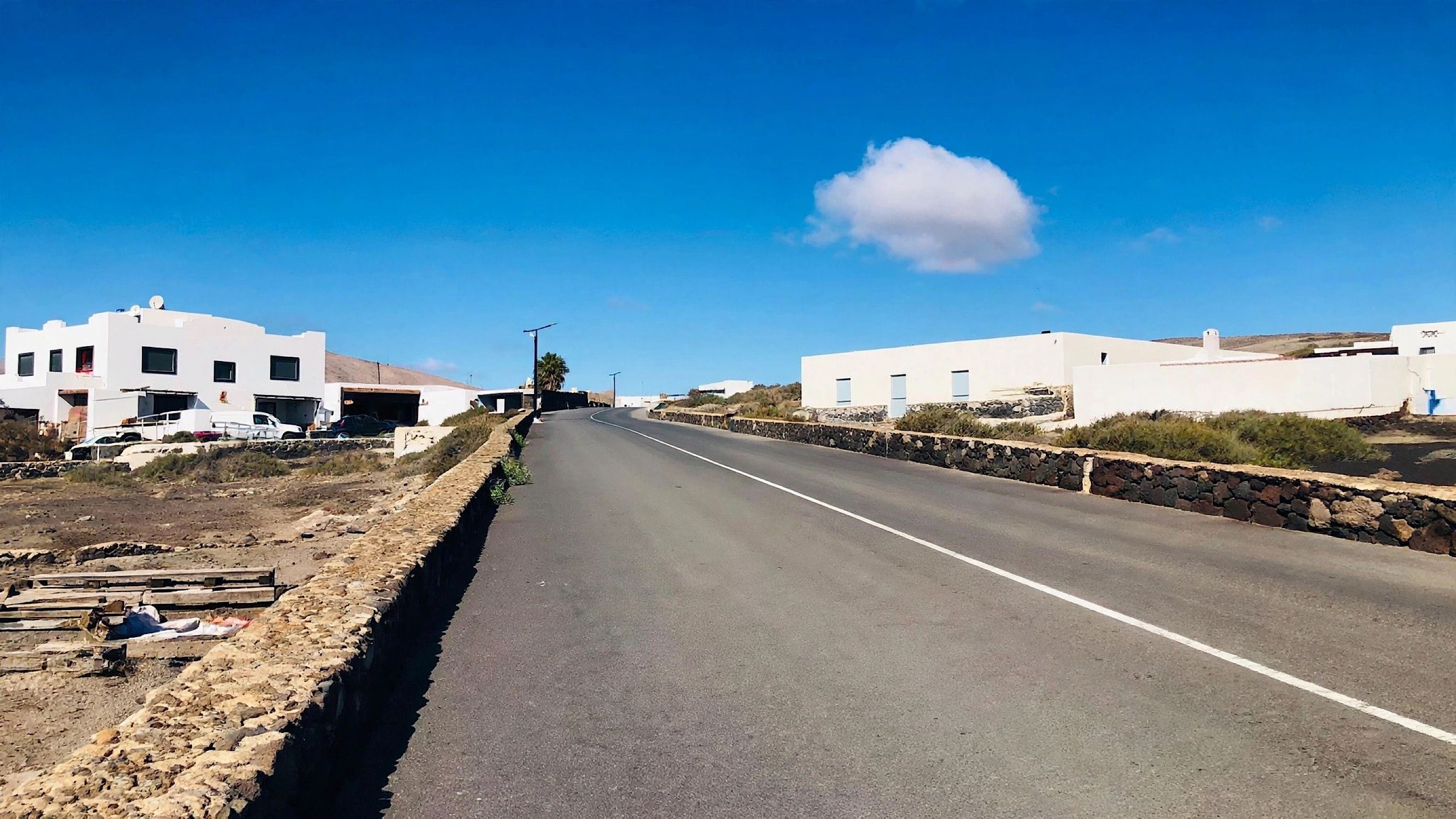 Eine gerade Straße, gesäumt von weißen Gebäuden mit Steinmauern, unter blauem Himmel.