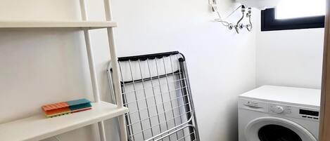 A laundry room with a washing machine, a drying rack, and a shelf with books.