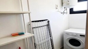 Una lavanderia con lavatrice, stendibiancheria e uno scaffale con libri.